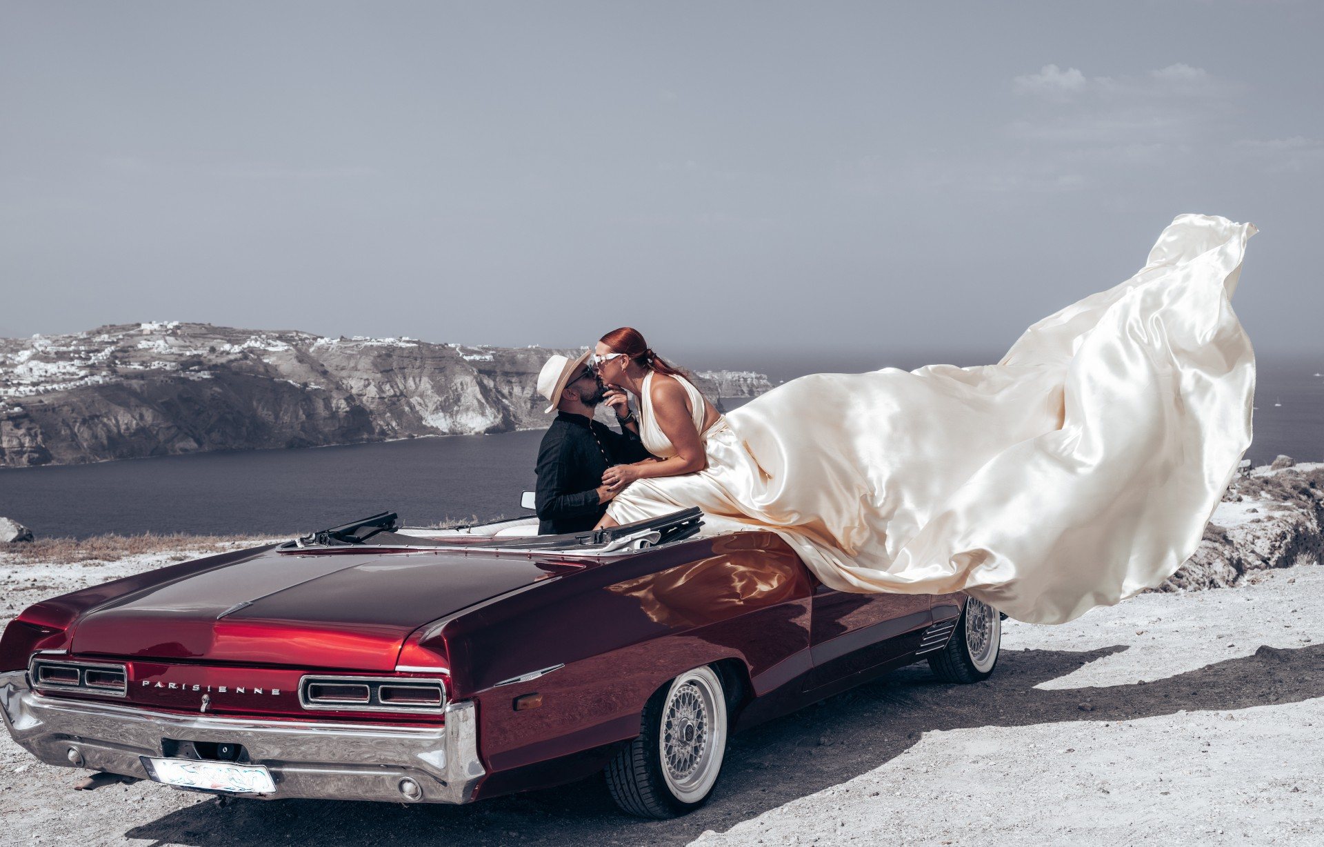 Marriage proposal photoshoot in Santorini - flying dress on the vintage Pontiac Parisienne above the caldera